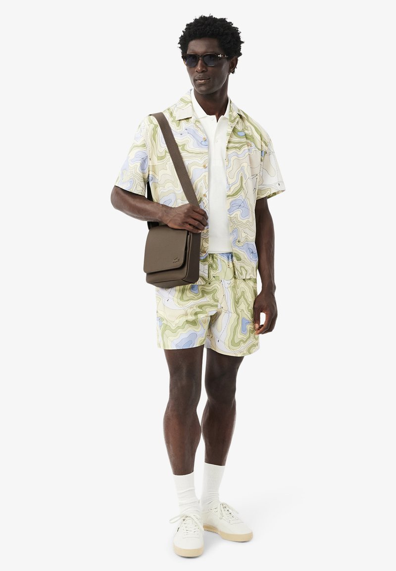 Ensemble chemise à manches courtes et short en motif marbré vert pastel et bleu, accompagné d'un t-shirt blanc, de baskets crème et d'un sac bandoulière marron.