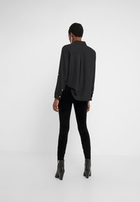 Chemise noire à manches longues avec une coupe ample, présentant des détails de boutons aux poignets, associée à un pantalon noir ajusté et des bottines à talons.