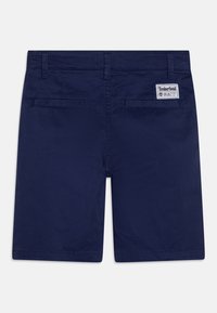 Shorts bleu marine avec une texture lisse, deux poches arrière et une étiquette avec le logo Timberland sur la taille. Forme rectangulaire, bords ourlés.