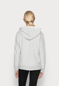 Sudadera con capucha gris claro, con una textura suave, ajuste relajado, puños acanalados y un bolsillo tipo canguro. Vista trasera que muestra la capucha y detalles de costura.