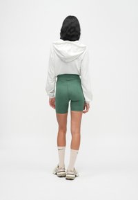 Γκρι cropped φούτερ με κορδόνι, συνδυασμένο με πράσινα σορτς ψηλόμεσα. Λευκές κάλτσες μέχρι το γόνατο με μαύρο λογότυπο και ανοιχτόχρωμα αθλητικά παπούτσια.