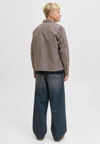 Brun rutig jacka med krage, bärs över en svart skjorta, tillsammans med vida blå denimjeans. Outfiten har en avslappnad passform.