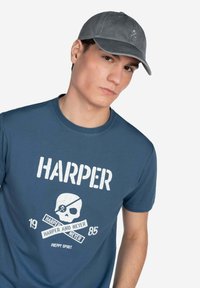 Camiseta de algodón azul con texto blanco y un gráfico de calavera; acompañada de una gorra gris con un pequeño diseño bordado.