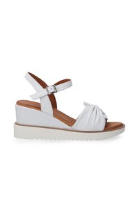 Witte wedge sandaal met een gecapitonneerde stofknoopdetail, enkelbandje en een contrasterende rubberen zool. Heeft een bovenwerk van soepel leer.