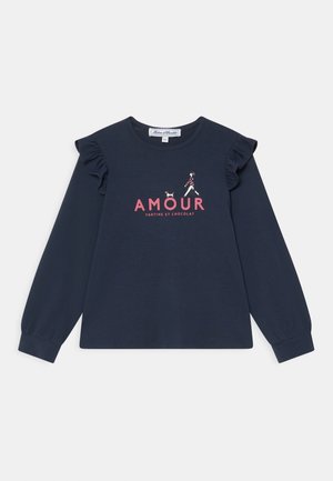 Marineblå langærmet skjorte med flæseærmer, lyserød "AMOUR" tekst og illustration af en pige, der går tur med en lille hund ovenover teksten.