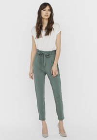 Lightweight, green fabric trousers with a high waist, belt tie and slim-fit tapered legs; paired with a short-sleeve white top and beige heels.