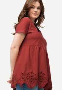 Top de algodón rojo con mangas cortas, un torso ajustado, dobladillo acampanado y borde de encaje bordado en la parte inferior. Textura suave, diseño casual.