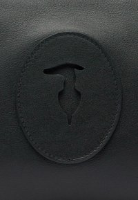 Accessorio in pelle nera con un logo circolare in rilievo e un design a fori al centro. Texture liscia con cuciture dettagliate.