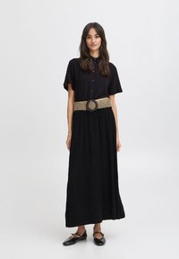 Robe maxi noire à manches courtes, avec un devant boutonné et une ceinture texturée à rayures mettant en valeur une boucle ronde. Tissu lisse et design fluide.