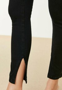 Czarne dżinsy o długości kostki z rozcięciem po bokach i dopasowanym kroju, o gładkiej fakturze i minimalnych detalach szwów.