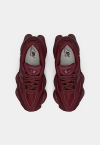 Bordeaux hardloopschoenen van mesh en suède, met opvallende veters, een gebogen zoolontwerp en reflecterende accenten.