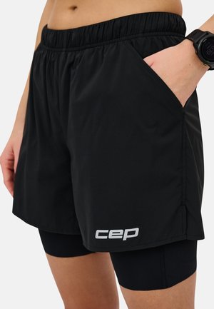 Schwarze Sportshorts mit elastischem Bund, Seitentaschen und einer längeren äußeren Schicht über enganliegenden schwarzen Shorts, mit einem weißen Logo.
