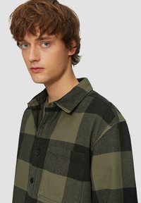 Groen en zwarte geruite shirt, gemaakt van stof, met een kraag, knopen aan de voorkant en een borstzak. Zichtbare textuur in het geweven patroon.
