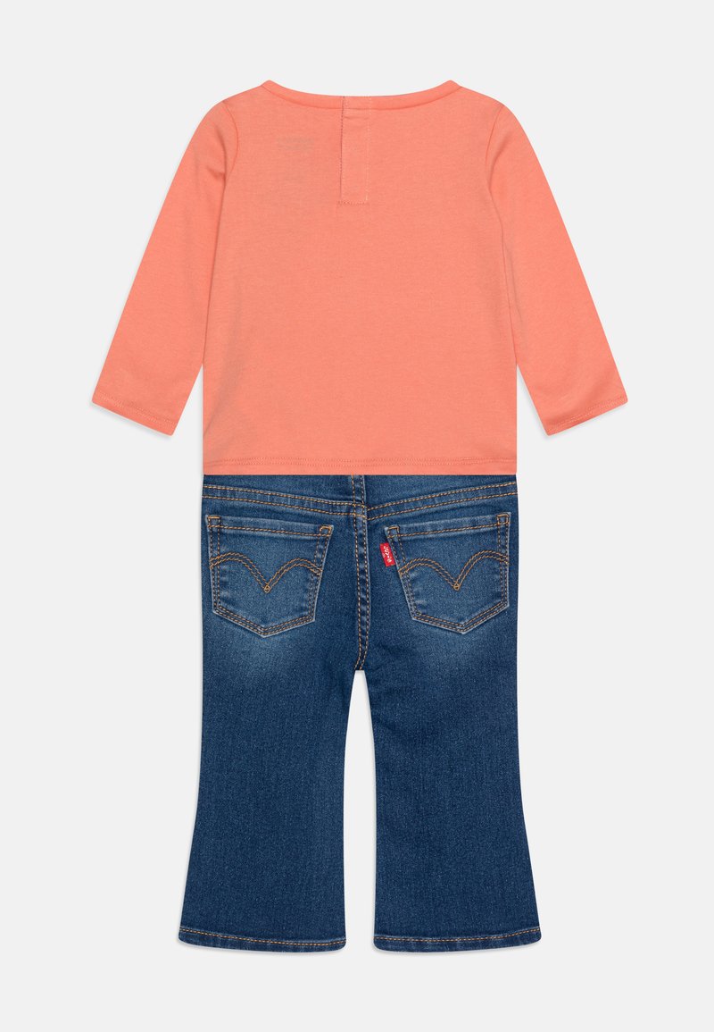 Maglietta a maniche lunghe color corallo con scollatura rotonda abbinata a pantaloni di jeans blu a zampa d'elefante con tasche posteriori e dettagli di cucitura distintivi.