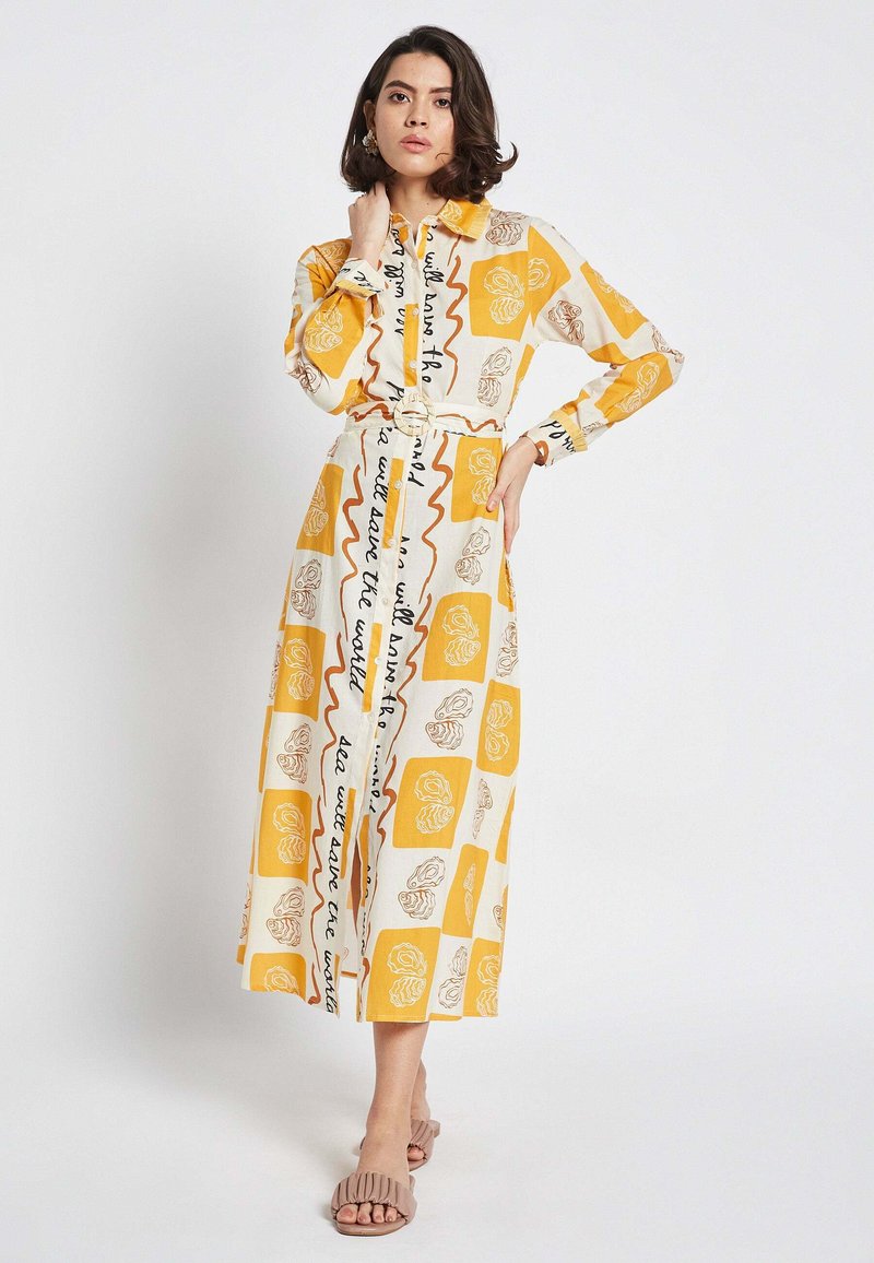 Long button-up dress with a yellow and white pattern featuring abstract designs and text. Lightweight fabric, belted at the waist.