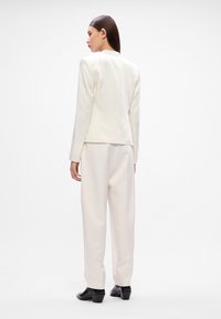 Blazer branco bem cortado e calças combinando em tecido suave. Corte slim, ombros estruturados e um brilho sutil. Sapatos de salto pretos complementam o visual.