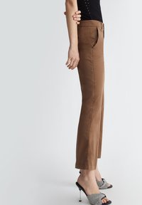 Pantaloni marroni a gamba dritta con una texture liscia, dotati di tasche laterali e vita media, abbinati a sandali neri con tacco alto.