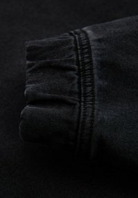 Mustekankainen farkkukangas, jossa on kerätty hihansuu, näkyviä ompeluyksityiskohtia saumoissa ja sileä pinta kauttaaltaan.