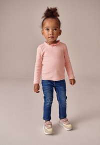 Hele roosa pika varrukaga pluus volangidega kaelusel, kombineeritud siniste teksade ja beežide tossudega, millel on roosad detailid ning valged tallad.