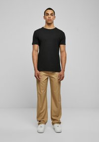 Black cotton t-shirt, round neckline, short sleeves, paired with beige pleated trousers, completing the look with white sneakers.