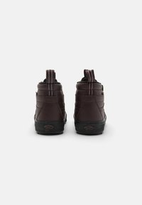 Brune høye sneakers med teksturert lær, polstret krage, trekkremmer og svarte gummisåler. Har kontrastsøm og logodetalj.