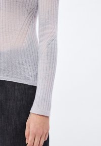 Lahka, prosojna pletena majica z gradiensom svetlo sive do nežno rožnate barve. Ima rebrasto teksturo in dolge rokave, s prilagojeno obliko.