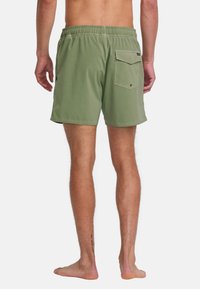 Shorts de bain verts avec une taille élastique, une poche arrière et une coupe courte et ajustée. Le matériau semble lisse avec une texture mate.