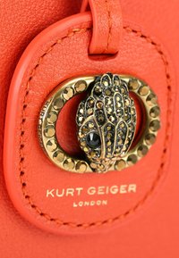 Pomarańczowa skórzana torebka o fakturowanej powierzchni, z zapięciem w kolorze złotym ozdobionym ciemnymi kamieniami szlachetnymi oraz wytłoczonym napisem "Kurt Geiger London".
