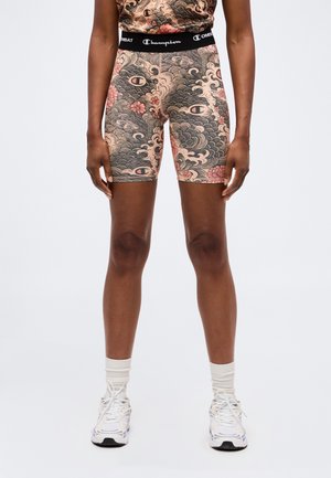 Vue de face d'une personne portant un short Champion à motifs floraux et ondulés, avec une ceinture élastique noire et des baskets blanches avec des chaussettes.