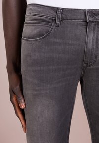 Gray denim jeans with a smooth texture, featuring a classic fit, subtle fades, and side pockets. Button closure at the waist.
