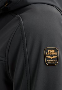 Black jacket featuring a smooth texture, with a prominent PME Legend patch in gold and black, positioned on the upper shoulder area.