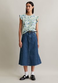 Bloemrijke top met korte mouwen en ruffle-details, gecombineerd met een high-waisted spijkerrok. Het model draagt zwarte schoenen met witte sokken.