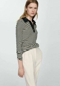Polo de rayas en blanco y negro con cuello negro y tapeta de botones. Combinado con pantalones claros y ajustados. Tejido suave.