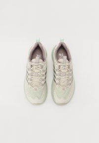 Baskets de sport beige clair avec une tige en maille texturée, des accents vert pâle et des bandes réfléchissantes. Dotées d'un design à lacets et d'un col rembourré.