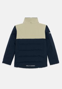 Veste isolante bleu marine et beige avec un col haut, texture matelassée et logo en bas. Elle dispose de manches longues et d'un design épuré.
