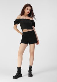 Sort cropped off-the-shoulder top med tekstureret detalje, parret med sorte denimshorts og skinnende sorte ankelstøvler med chunky såler.