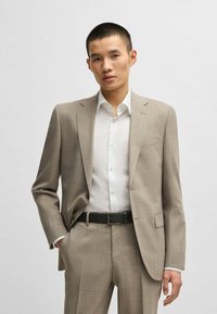 Abito checked marrone chiaro con vestibilità su misura e rever a scollo a V, abbinato a una camicia bianca. Cintura nera strutturata con fibbia in argento.