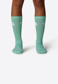 Calcetines de longitud hasta la rodilla en color turquesa, fabricados con material transpirable, que presentan una textura acanalada y un logo blanco en la parte frontal.