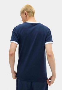 Camiseta de algodón azul marino con cuello y acentos en las mangas en blanco, con un corte holgado y textura suave, vista desde la parte de atrás.