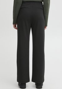 Pantalons larges noirs fabriqués en tissu lisse, dotés d'une taille haute, de deux poches arrière et d'un design ajusté pour une silhouette structurée.
