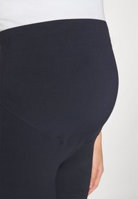 Leggings neri elasticizzati con vita alta, caratterizzati da una texture liscia e cuciture modellanti che creano una silhouette aderente.