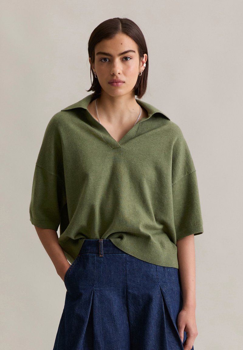 Zielony, oversize'owy sweter z dekoltem w serek i krótkimi rękawami, połączony z ciemnoniebieską spódnicą z wysokim stanem z denimu, z plisami.