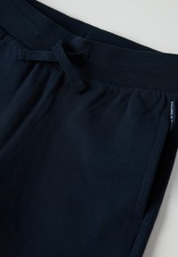 Marine joggers gemaakt van zacht materiaal, met een elastische tailleband met trekkoord, zijzakken en een klein merklabel aan de zijkant.