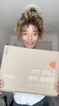 Caixa de papelão segurada por uma pessoa, apresentando uma cor castanha clara com texto branco que diz "Ama-me. Usa-me." e um pequeno destaque laranja.