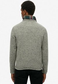 Suéter de punto gris con cuello alto, que presenta un interior de cuadro de colores. Puños y dobladillo acanalados, tejido texturizado con motas.