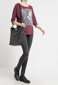 Burgundy long-sleeve shirt with graphic print, paired with gray fitted jeans and black lace-up shoes. A black shoulder bag with a chain accent.