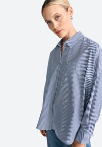 Button-up shirt in cotton, featuring blue and white vertical stripes. Loose fit, with a chest pocket and classic collar. Soft texture.