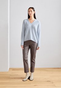 Helles blaues Strickpullover mit V-Ausschnitt, kombiniert mit braunen Slim-Fit-Hosen und beigen Knöchelstiefeln mit quadrater Spitze und Blockabsatz.