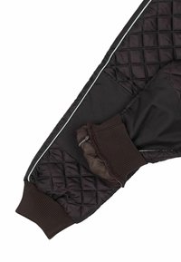 Sección de chaqueta negra acolchada con puño acanalado, textura suave y ribete claro en contraste a lo largo de la costura.