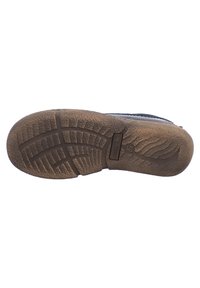 Hnědá gumová podešev obuvy s texturovaným vzorem podešve, který obsahuje drážky a detaily loga. Část podešve se mírně zvedá.